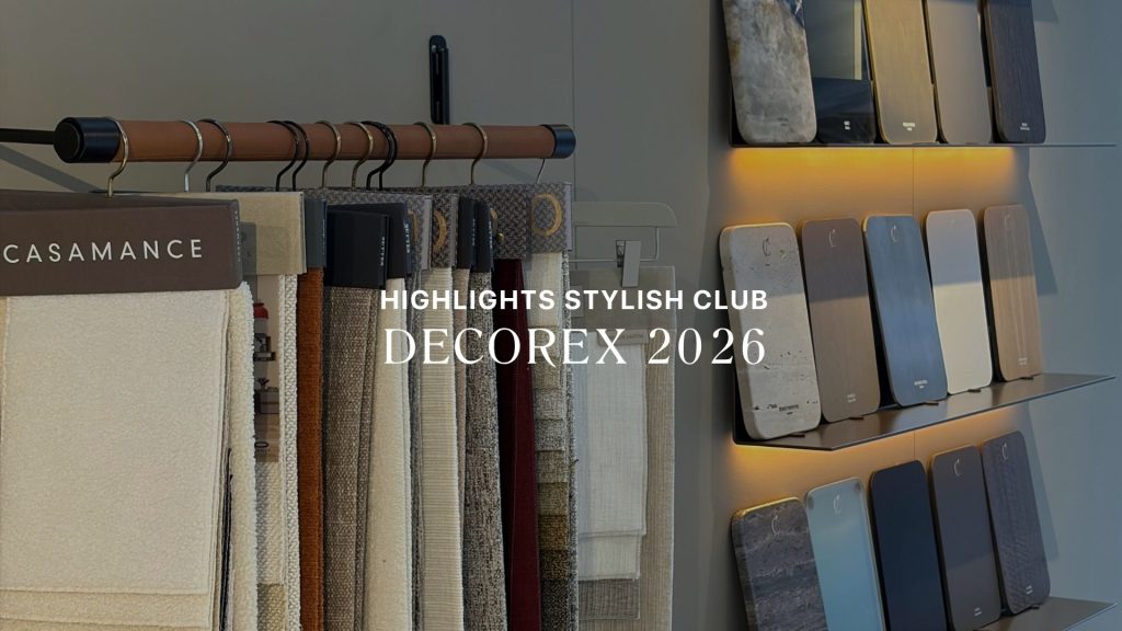 A close-up banner image displaying overlay text "HIGHLIGHTS STYLISH CLUB DECOREX 2026" against hanging fabric swatches and illuminated shelves of finish samples. Part of Stylish Club's Rare Matter presentation, the display offers high-end furniture luxury design, rich furniture upholstey fabric, and refined options for bespoke furniture solutions.
