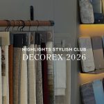 A close-up banner image displaying overlay text "HIGHLIGHTS STYLISH CLUB DECOREX 2026" against hanging fabric swatches and illuminated shelves of finish samples. Part of Stylish Club's Rare Matter presentation, the display offers high-end furniture luxury design, rich furniture upholstey fabric, and refined options for bespoke furniture solutions.