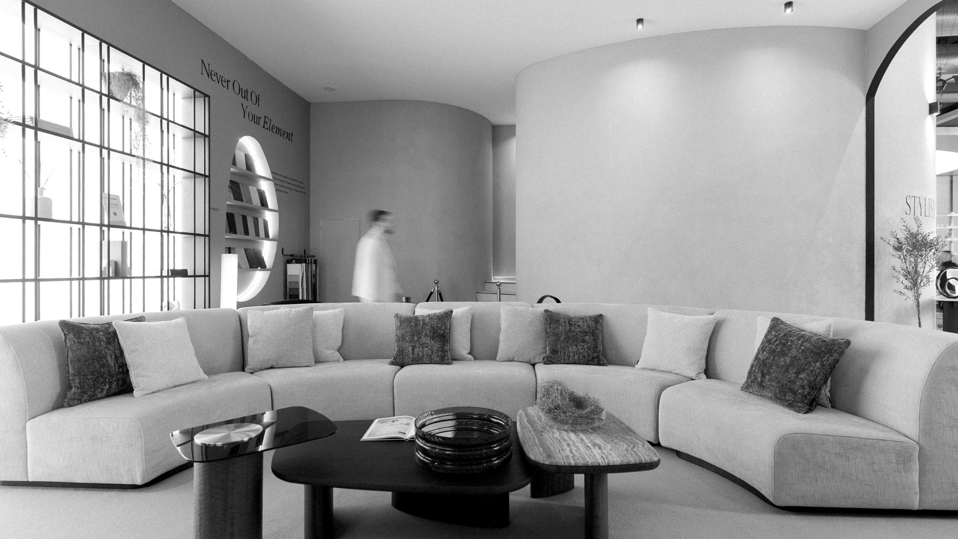 A curved modular sectional sofa and modern coffee tables arranged inside a contemporary exhibition booth, showcasing luxury living room furniture and furniture luxury design ideal for high-end hospitality designs.
