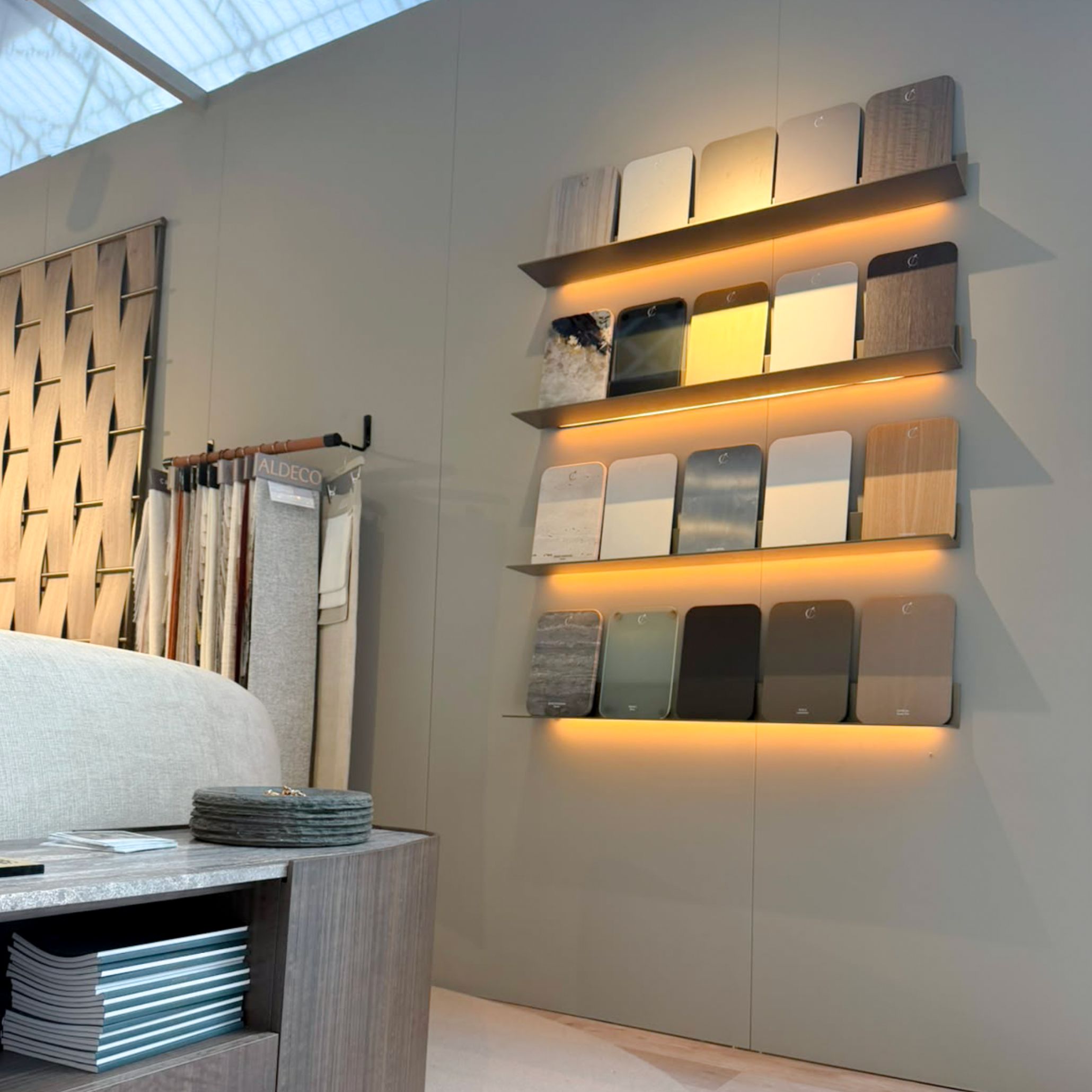 A serene wellness lounge corner inside Stylish Club’s stand at Decorex 2026, featuring a curved textured chair, dark wood finishes, and hanging linen banners with design sketches. The booth provides living room inspiration through tactile design details and custom furniture tailored for restorative, modern interiors.