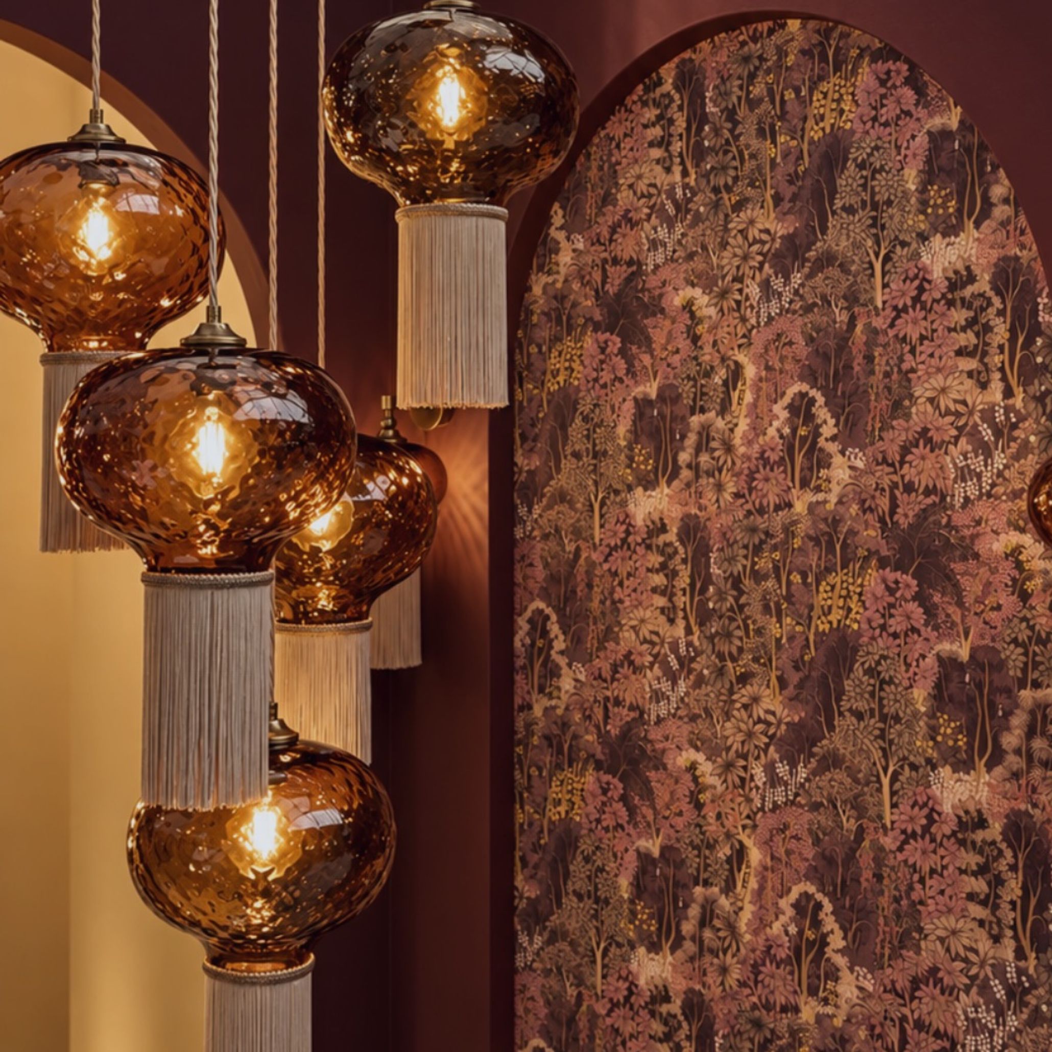 Warm-toned amber glass pendant lights with delicate tassels hang in front of rich terracotta walls and patterned botanical wallpaper. This setting showcases interior design inspiration and artistic design details that bring depth, warmth, and character to modern living room design.