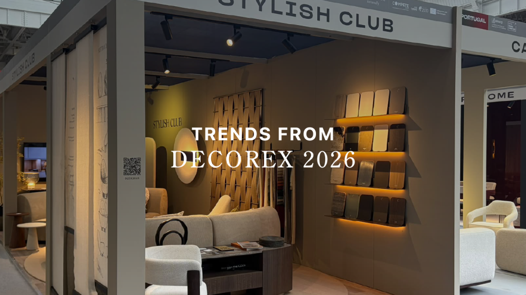 Stylish Club’s exhibition stand at Decorex 2026 featuring the title text "TRENDS FROM DECOREX 2026" overlaid across an warm interior display. The booth showcases plush modular seating, illuminated finish swatches, and organic wood paneling, offering sophisticated interior design inspiration, bespoke furniture solutions, and high-end custom furniture.
